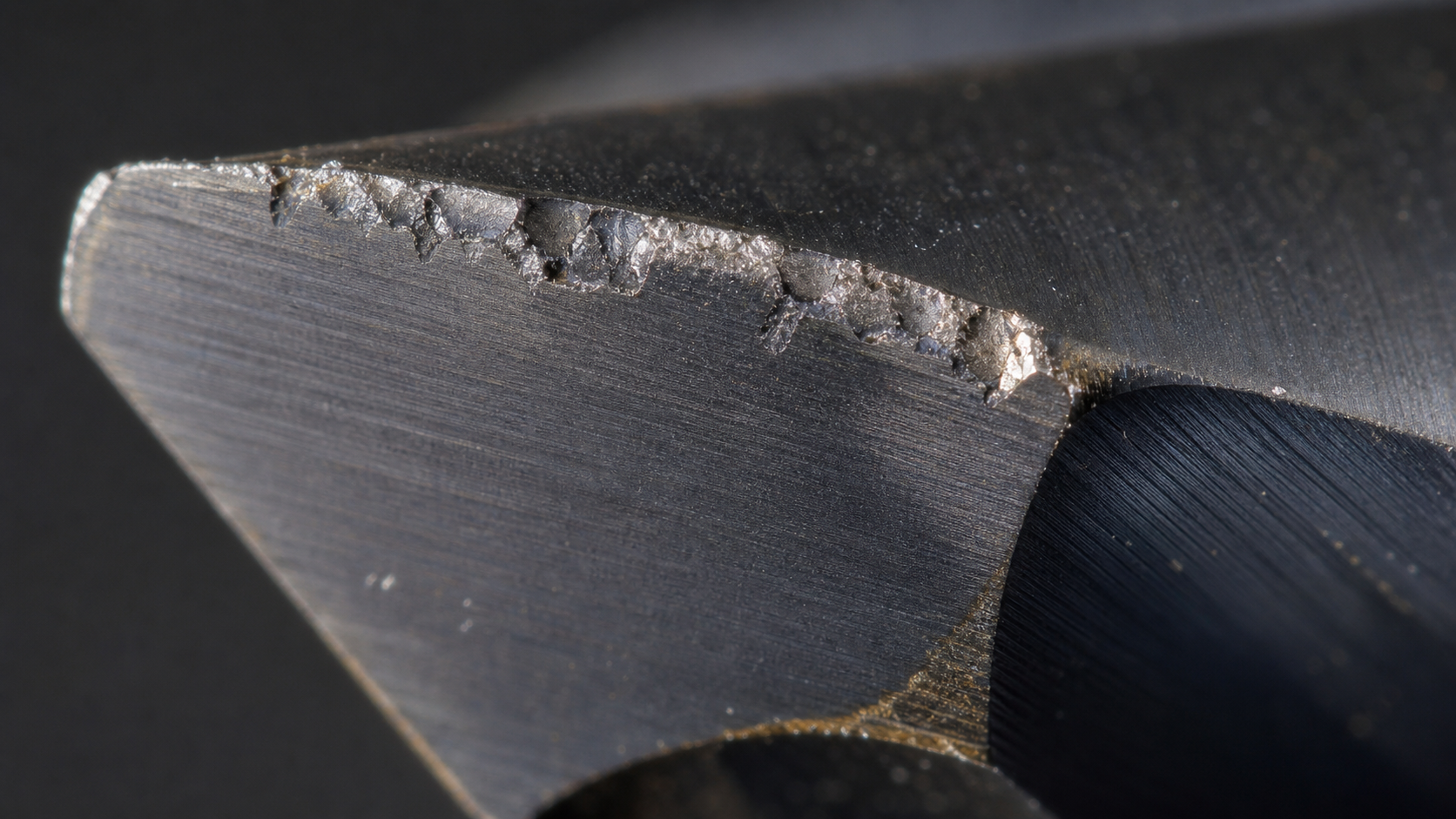A magnified view of a carbide cutting tool's edge showing microscopic chipping and wear after machining a glass-filled polymer