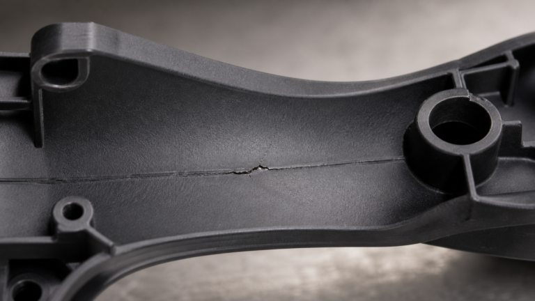 A close-up view of a cracked black PPS component showing the failure point along a subtle weld line.