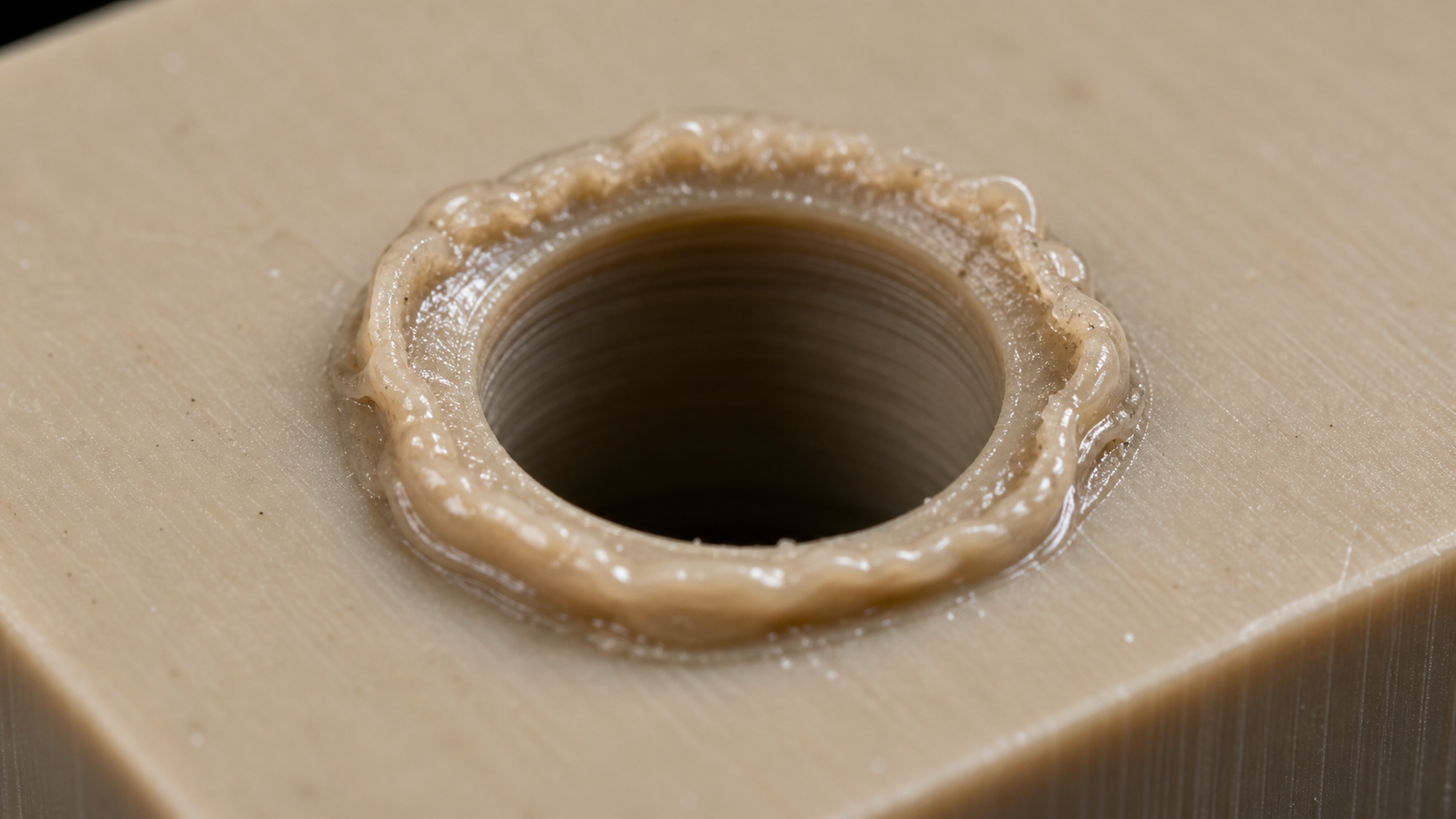 Identifying Local Heat Damage in Drilled PEEK A magnified view of a poorly drilled hole in a PEEK component, highlighting the raised, melted burr on the surface.